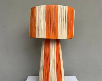 May include: A tall, orange and white striped table lamp with a wide, cylindrical base and a conical shade.