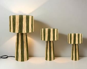 May include: Three striped table lamps with green and beige stripes. The lamps are different sizes, with the largest lamp in the back and the smallest lamp in the front.