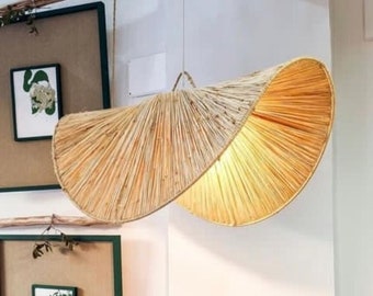 May include: A woven, light brown, fan-shaped pendant light fixture with a unique, curved design. The light fixture is hanging from the ceiling and is illuminated.