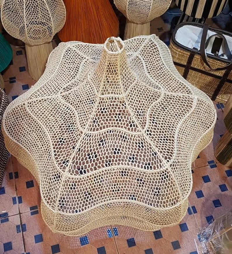 May include: A large, star-shaped woven basket in natural beige tones. The basket has a unique, open-weave design with a central, cylindrical opening. Other woven items are visible in the background, suggesting a home decor theme.