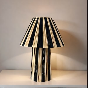 May include: A black and cream striped lamp with a cylindrical base. The lampshade is made of woven rope and has a pleated design.