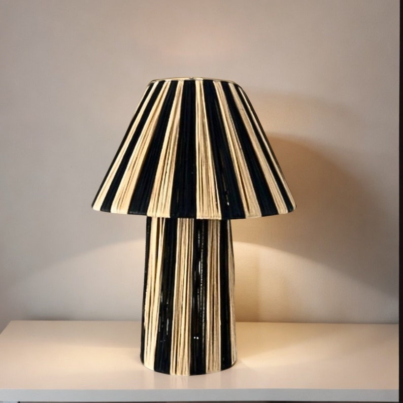 May include: A black and cream striped lamp with a cylindrical base. The lampshade is made of woven rope and has a pleated design.