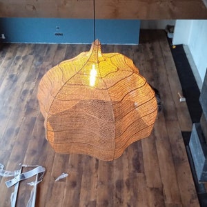 May include: An overhead shot of a woven, spherical pendant light. The light emits a warm orange glow. The fixture hangs above a wooden floor. The room has a modern design with a fireplace and a blue wall.