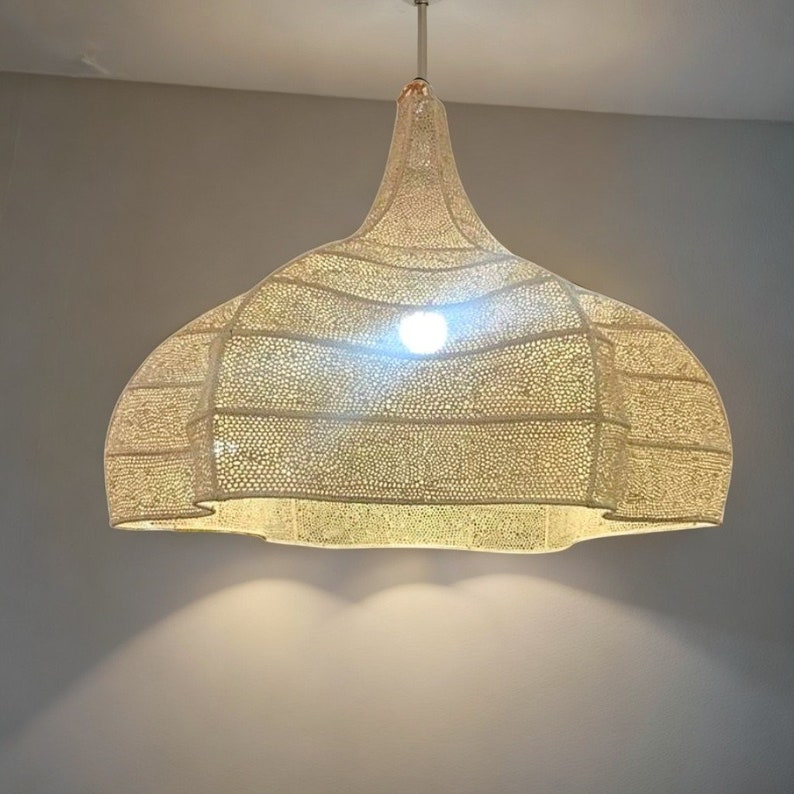 May include: A cream-coloured, dome-shaped pendant light fitting. The light has a perforated design, allowing light to filter through. The fitting is suspended from the ceiling by a thin, silver rod.