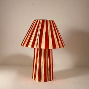 May include: A red and white striped table lamp with a pleated lampshade. The lamp has a cylindrical base.