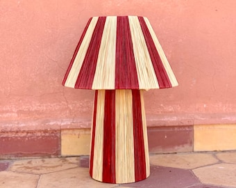May include: A red and white striped lamp with a wide, conical shade and a tall, cylindrical base. The lamp is made of woven material and has a rustic, handmade look.