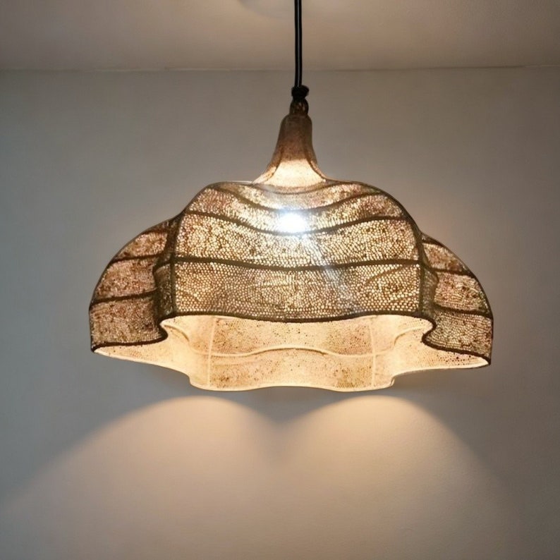 May include: A decorative pendant light with a distinctive lampshade. The lampshade has a layered, ruffled design with a speckled, light brown and beige colour scheme. The light fixture hangs from a black cord.