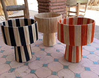 May include: Three table lamps with striped shades. The shades are made of woven natural fibers and are striped in black and white, orange and white, and natural and white. The lamps are on a tiled floor.