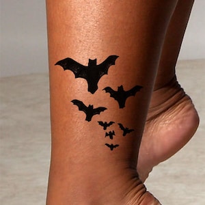 May include: A temporary tattoo featuring a design of several black bats in flight. The tattoo is applied to a person's ankle.