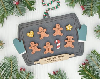 May include: A dark gray wooden baking sheet ornament featuring four gingerbread person shapes labeled Mandy, Joey, Blake, and Nora, a dog shape labeled Margo, a yellow star, a heart, and a candy cane. A rolling pin reads JACKSON FAMILY RECIPE CHRISTMAS 2026.