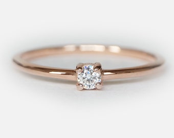 May include: A delicate rose gold band ring with a single, small, round diamond set in the center.