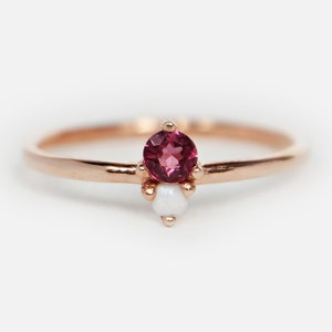Puede incluir: Un delicado anillo de oro rosa con una piedra preciosa rosa y dos acentos de ópalo blanco.