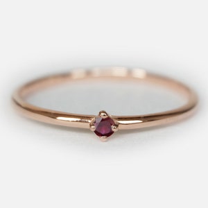 Puede incluir: Un delicado anillo de oro rosa con una sola piedra preciosa roja pequeña engastada en el centro.