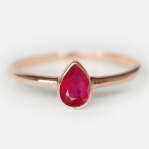 Könnte beinhalten: Ein Ring aus Roségold mit einem rubinroten Edelstein in Tropfenform. Der Ring ist schlicht und elegant.