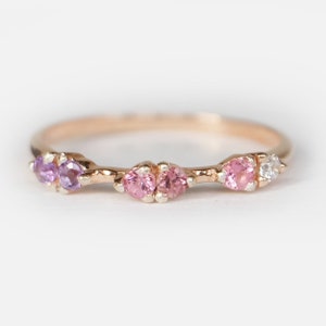 May include: A delicate gold band ring featuring a row of three pink and one purple gemstones. The ring has a minimalist design and is ideal for everyday wear.