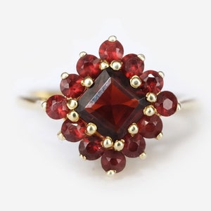 May include: A gold ring with a large, square-shaped red garnet surrounded by smaller red garnets.