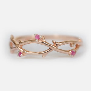 May include: A delicate rose gold ring with a twig design and three small pink gemstones.