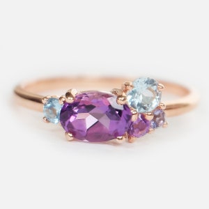 May include: A rose gold ring with a large oval amethyst gemstone surrounded by smaller amethyst and aquamarine gemstones.