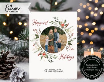 May include: A white Christmas card with a watercolor wreath of greenery, berries, and flowers. A circle in the center of the wreath contains a photo of a family of four. The text "Happiest Holidays" is written in red cursive script. The text "With love from, The Halpert Family" is written in black at the bottom of the card.