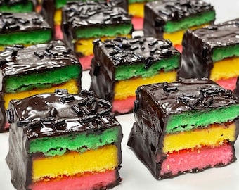 May include: A collection of square-shaped petit fours arranged in rows. Each treat features three distinct horizontal layers of cake in green, yellow, and pink, fully coated in a dark chocolate glaze and topped with small dark chocolate sprinkles.