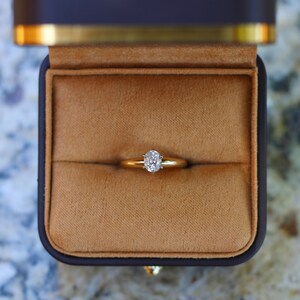May include: A gold ring with a single, round, clear diamond in a simple setting. The ring is in a brown velvet ring box.