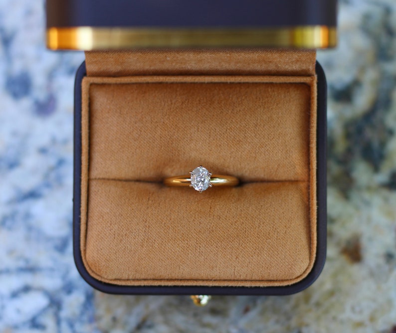 May include: A gold ring with a single, round, clear diamond in a simple setting. The ring is in a brown velvet ring box.