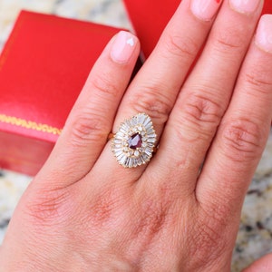 May include: A gold ring with a pear-shaped red gemstone surrounded by smaller white gemstones.
