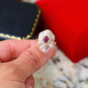 May include: A gold ring with a pear-shaped ruby surrounded by a halo of smaller diamonds.