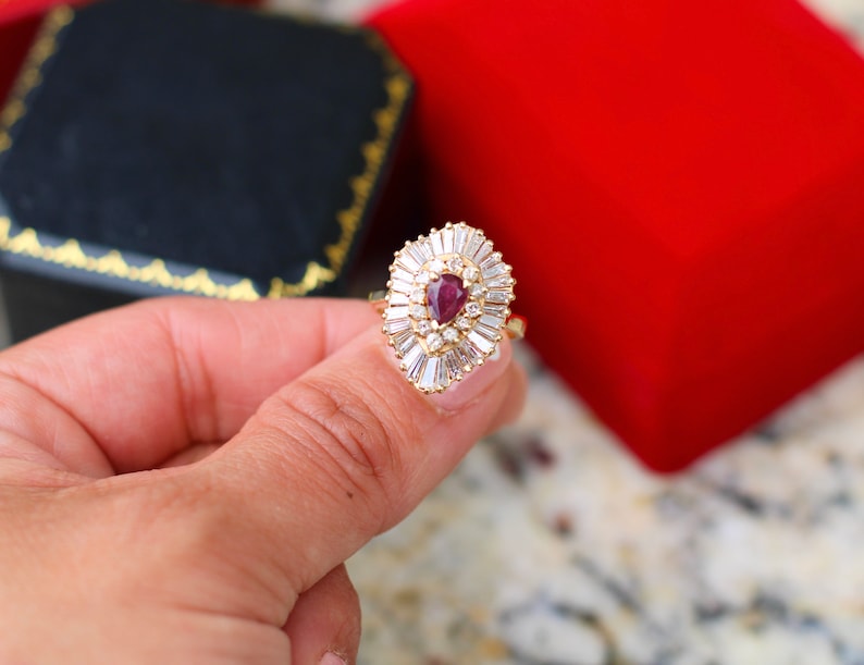 May include: A gold ring with a pear-shaped ruby surrounded by a halo of smaller diamonds.