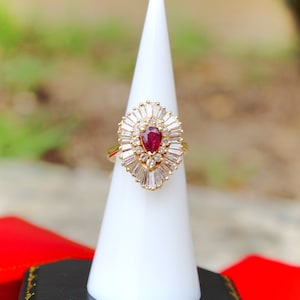 May include: A gold ring with a pear-shaped ruby surrounded by a halo of baguette-cut diamonds.