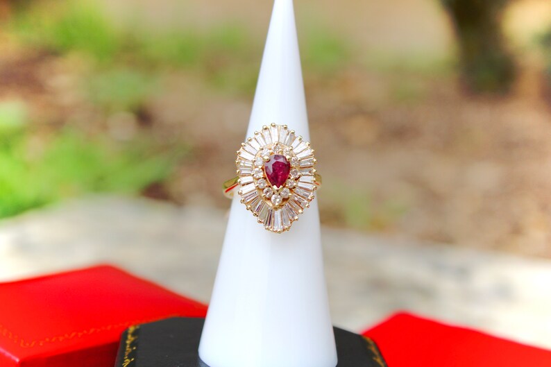 May include: A gold ring with a pear-shaped ruby surrounded by a halo of baguette-cut diamonds.