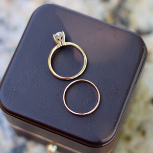 May include: Two gold wedding bands, one with a diamond, in a brown velvet ring box.