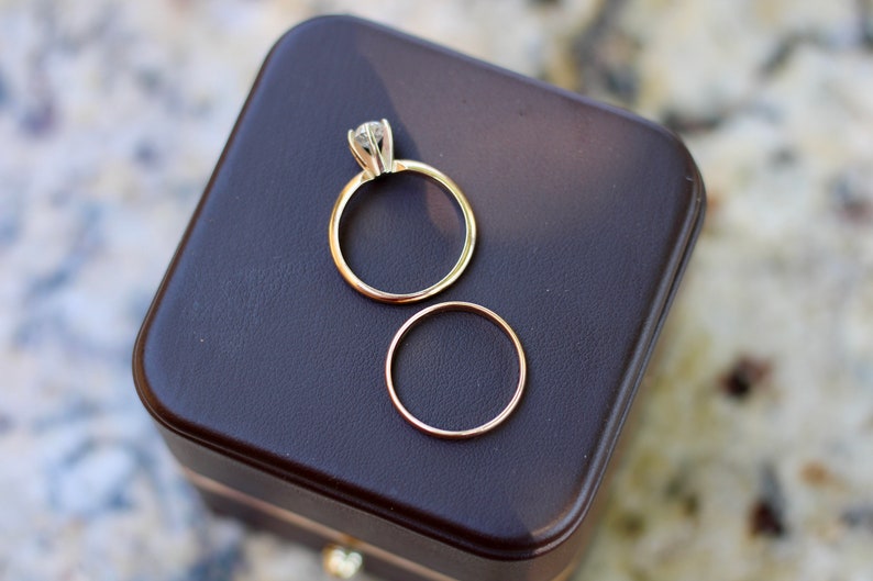 May include: Two gold wedding bands, one with a diamond, in a brown velvet ring box.