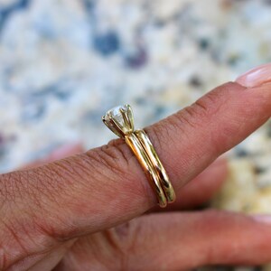 May include: A gold wedding band set with a large, round, clear diamond solitaire.