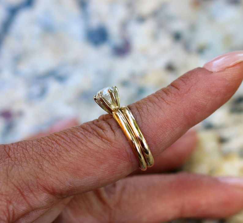 May include: A gold wedding band set with a large, round, clear diamond solitaire.