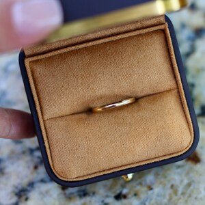 May include: A gold wedding band ring in a brown velvet ring box.