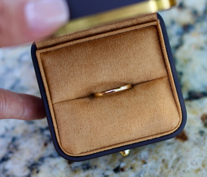 May include: A gold wedding band ring in a brown velvet ring box.