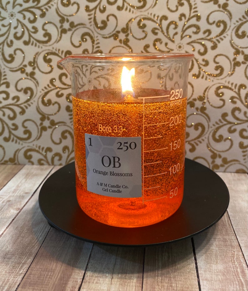 May include: A clear glass beaker candle with a label that reads "1 250 OB Orange Blossoms A & M Candle Co. Gel Candle". The candle is filled with a bright orange gel and has a single wick burning.