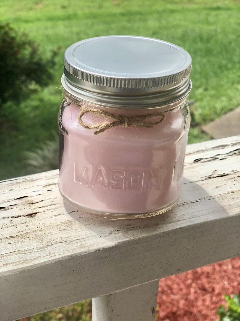 May include: A pink candle in a clear glass mason jar with a silver lid and a brown twine bow. The jar has the word "MASON" embossed on the side.