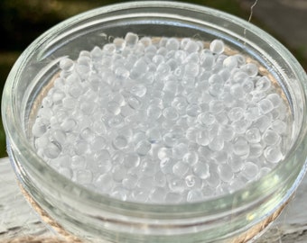 May include: A close-up of a glass jar filled with clear silica gel beads. The beads are small and round, and they are used to absorb moisture.