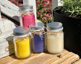 May include: Four small glass jars with silver lids and twine accents filled with colorful candles. The candles are yellow, purple, white, and pink.