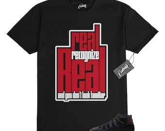 May include: Black t-shirt with red text that reads "real recognize real and you don't look familiar". A pair of black and red sneakers are in the bottom right corner of the image.