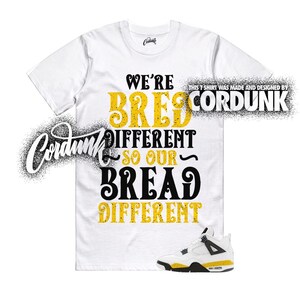 May include: A white short-sleeve t-shirt featuring the black and yellow text WE'RE BRED DIFFERENT SO OUR BREAD DIFFERENT. The shirt includes the brand name CORDUNK and a graphic of a white, black, and yellow athletic sneaker at the bottom right.