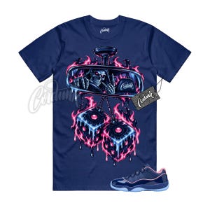 May include: A navy blue t-shirt featuring a graphic of a skeleton driving a car, seen through a rearview mirror, with pink and blue flames and hanging fuzzy dice. The text Cordunk is visible on the mirror, a tag, and the shirt collar.