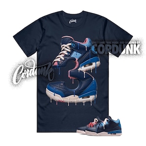 May include: A navy blue short-sleeve t-shirt featuring a graphic of a sneaker shaped like the number three with dripping paint effects in blue, pink, and white. The text Cordunk is printed on the shirt, and a pair of sneakers is shown at the bottom.