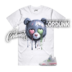 May include: White t-shirt featuring a distressed bear graphic with heart-shaped eyes in pink and green, and dripping paint. The shirt also has the text "CORDUNK" and a pair of white, pink, and green sneakers.