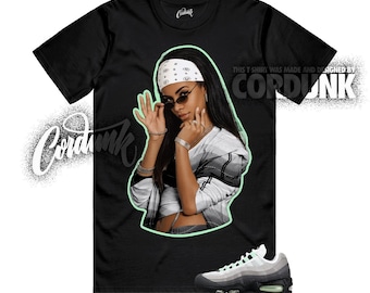 May include: Black t-shirt featuring a graphic of a woman wearing sunglasses and a white bandana. The text "CORDUNK" is printed on the shirt and in a stylized design on the left side. A pair of gray and black sneakers are at the bottom.