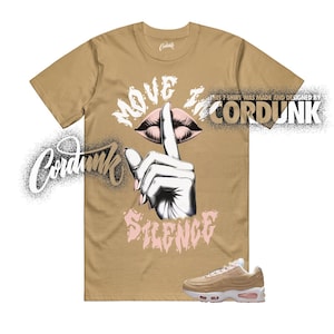 May include: A tan t-shirt featuring a graphic of a hand with a finger over lips, the text MOVE IN SILENCE, and the brand name CORDUNK. The shirt includes the text THIS T SHIRT WAS MADE AND DESIGNED BY CORDUNK. A tan and white sneaker is at the bottom.