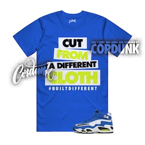 May include: A royal blue t-shirt with the text "CUT FROM A DIFFERENT CLOTH" in white and neon green. The shirt also features the text "#BUILTDIFFERENT". A pair of blue and white sneakers with the number 24 is at the bottom.