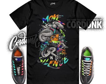 Peut inclure: T-shirt noir avec un motif de Méduse et le texte "MOVE IN SILENCE". Le design présente des serpents, des accents colorés et un visage stylisé. L'image comprend également une paire de baskets grises et colorées.